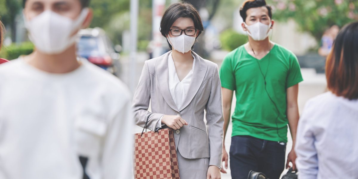 Beautiful young Asian woman in medical mask walking in the street in medical mask against viruses and diseases