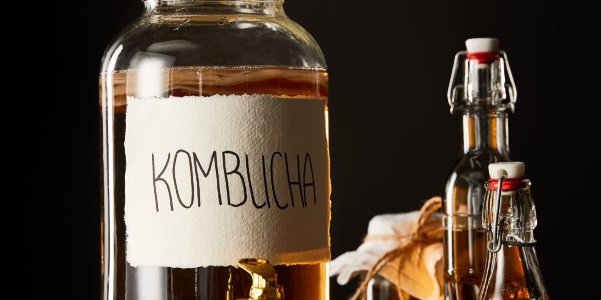 glass jar with kombucha near lemon, spice and bottles on wooden table isolated on black